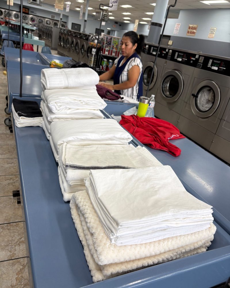 A team member folding laundry beside stacks of folded sheets and towels